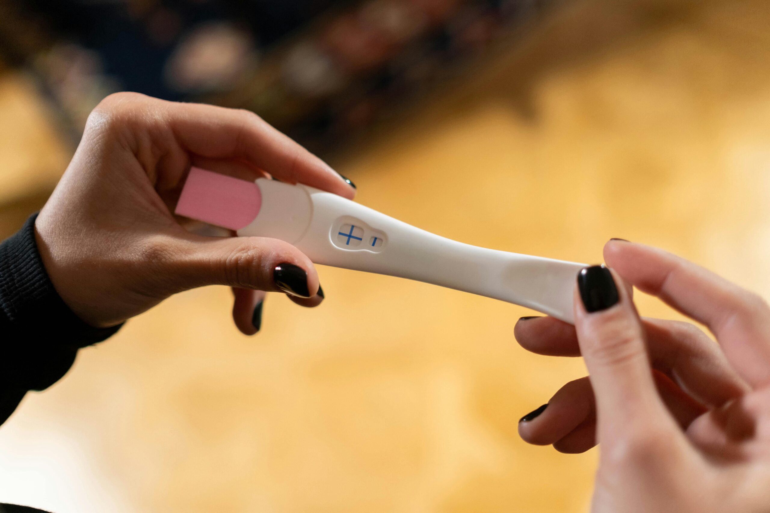 Closeup of hands holding a positive pregnancy test with a cross symbol.